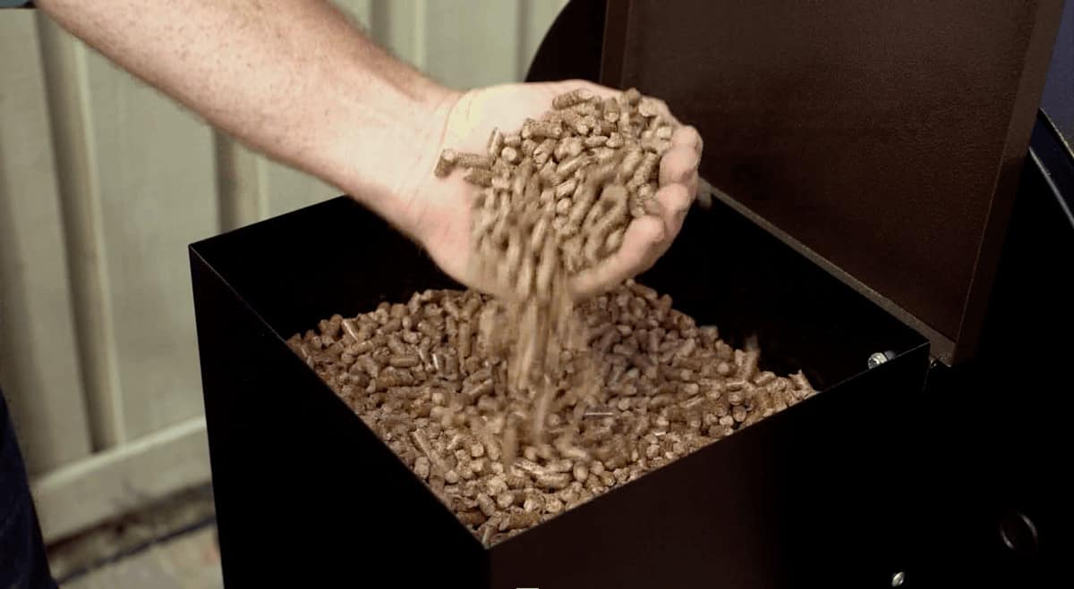 A handful of wood pellets held over a pellet grill hopp.