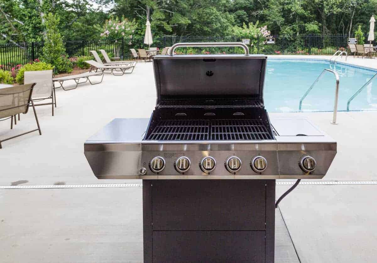 A new grill on a patio in front of a swimming p.