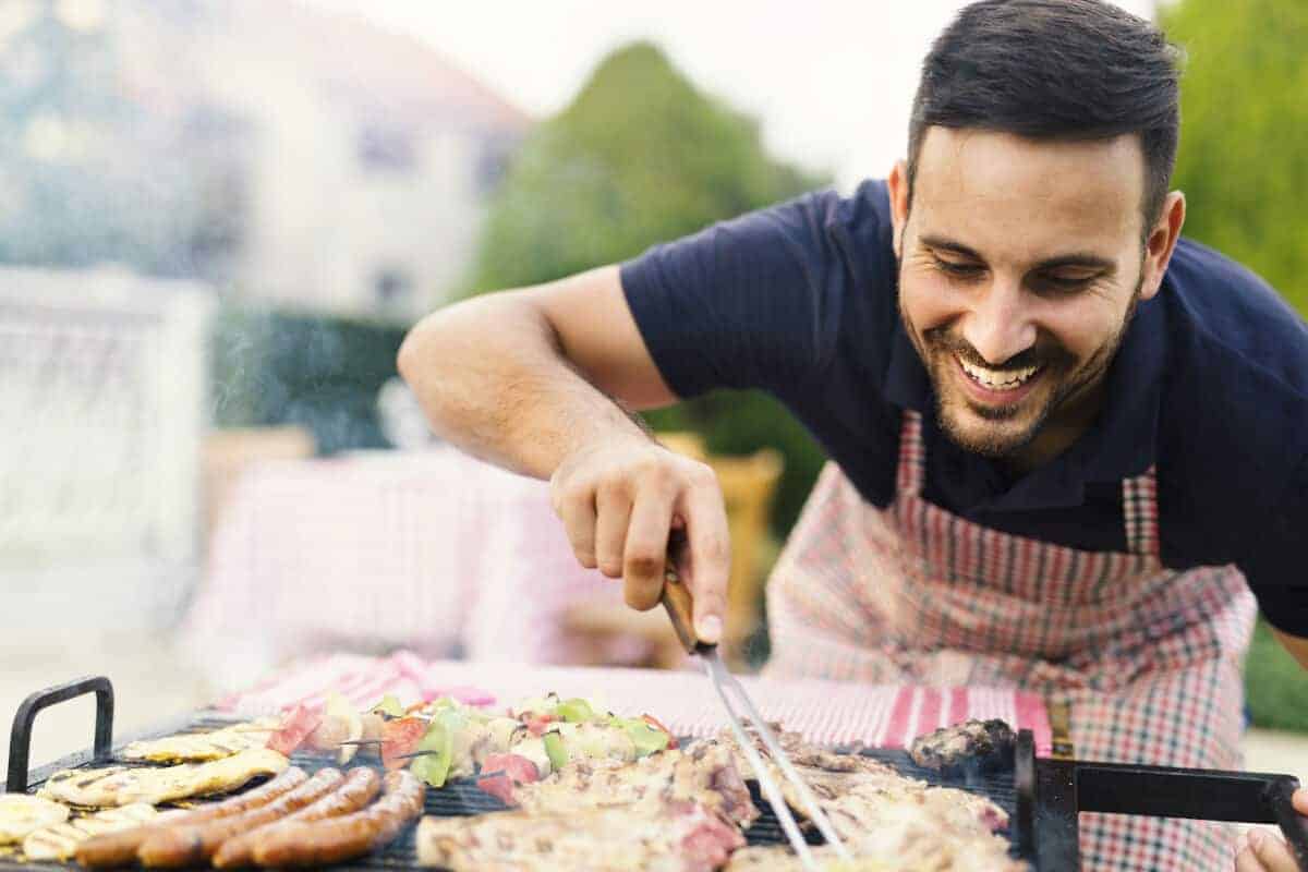 A happy looking man leaning over a BBQ turning m.