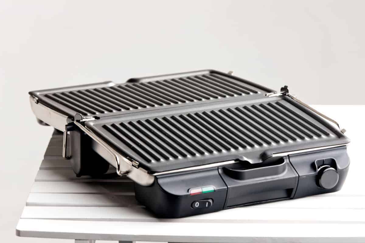 A small electric grill with lid open on a white ta.