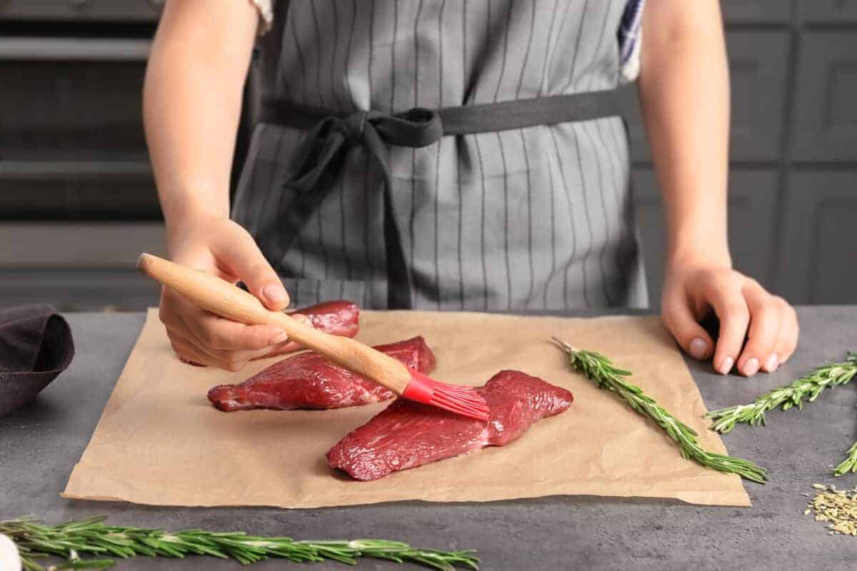 A woman oiling steaks on a chopping bo.