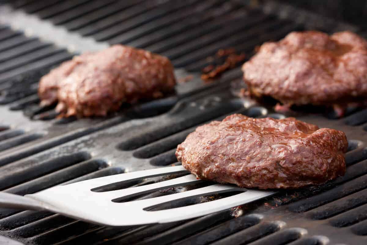 A spatula flipping burgers on a gas gr.