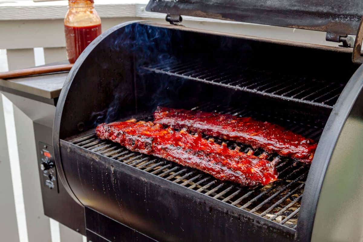 Two racks of pork ribs on a BBQ smoker, with smoke billow.