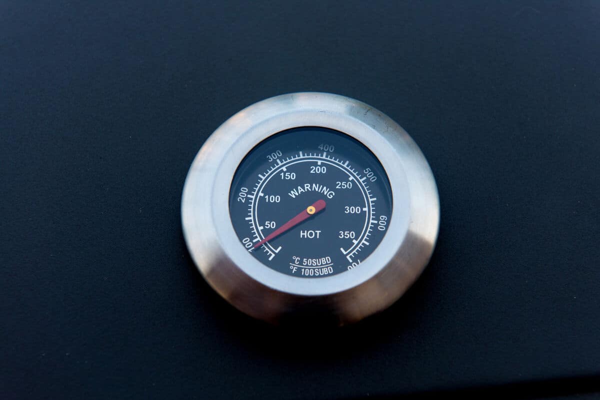 Close up of a BBQ lid thermometer on a black smo.