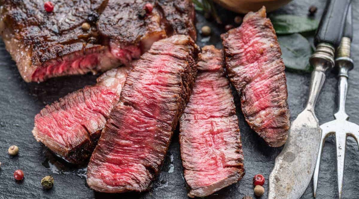 A medium rare grilled ribeye steak next to a sharp artisan knife on a chopping board.