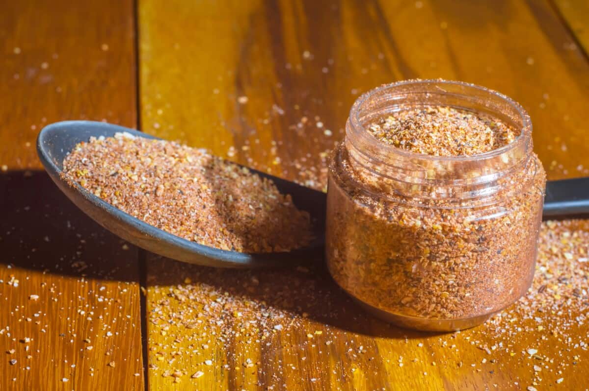 A jar and spoonful of home made BBQ dry rub on a wooden table.