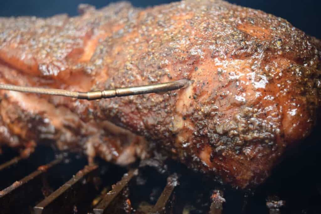 A smoker thermometer probe in a pork butt on a smo.