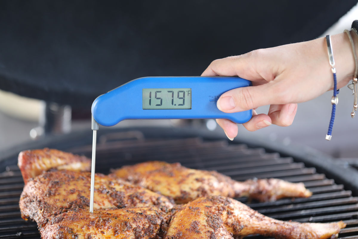Internal temperature of chicken on a grill being taken by an instant read thermometer in a woman's hand