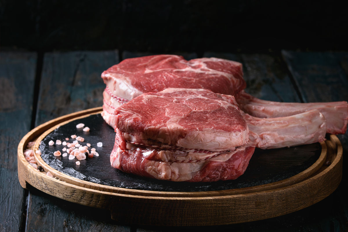 2 large tomahawk steaks sitting on a chopping board coming up to room t.