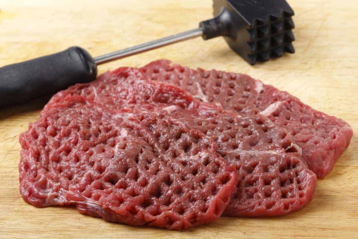 Tenderized steak on a chopping board with a mallet