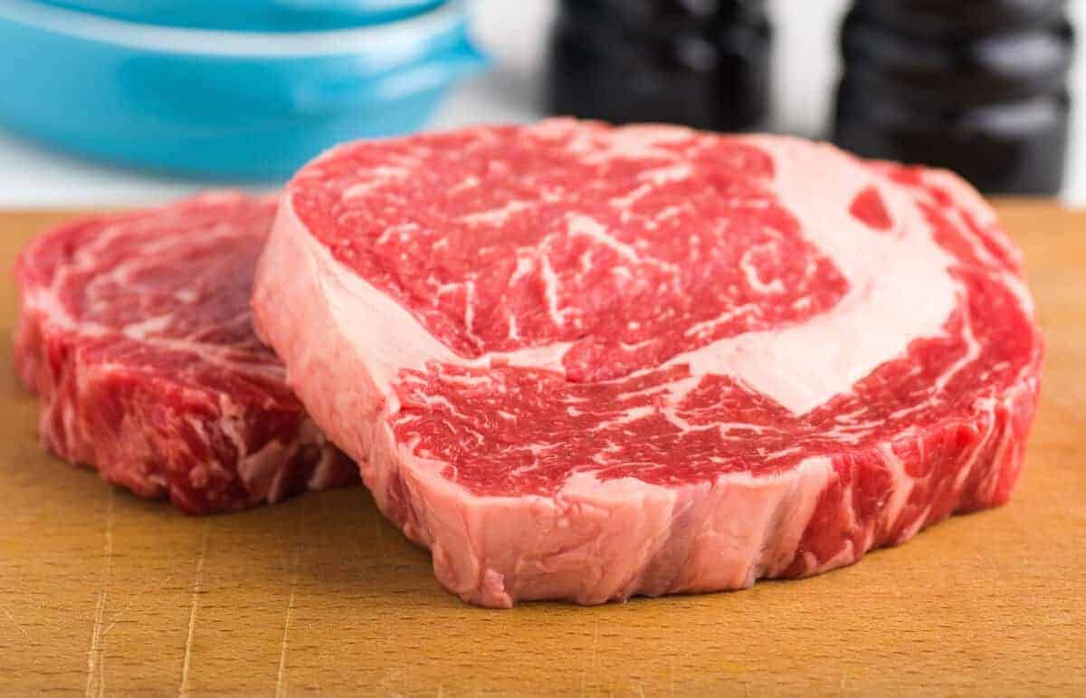 Two well-marbled rib eye steaks on a wooden cutting bo.