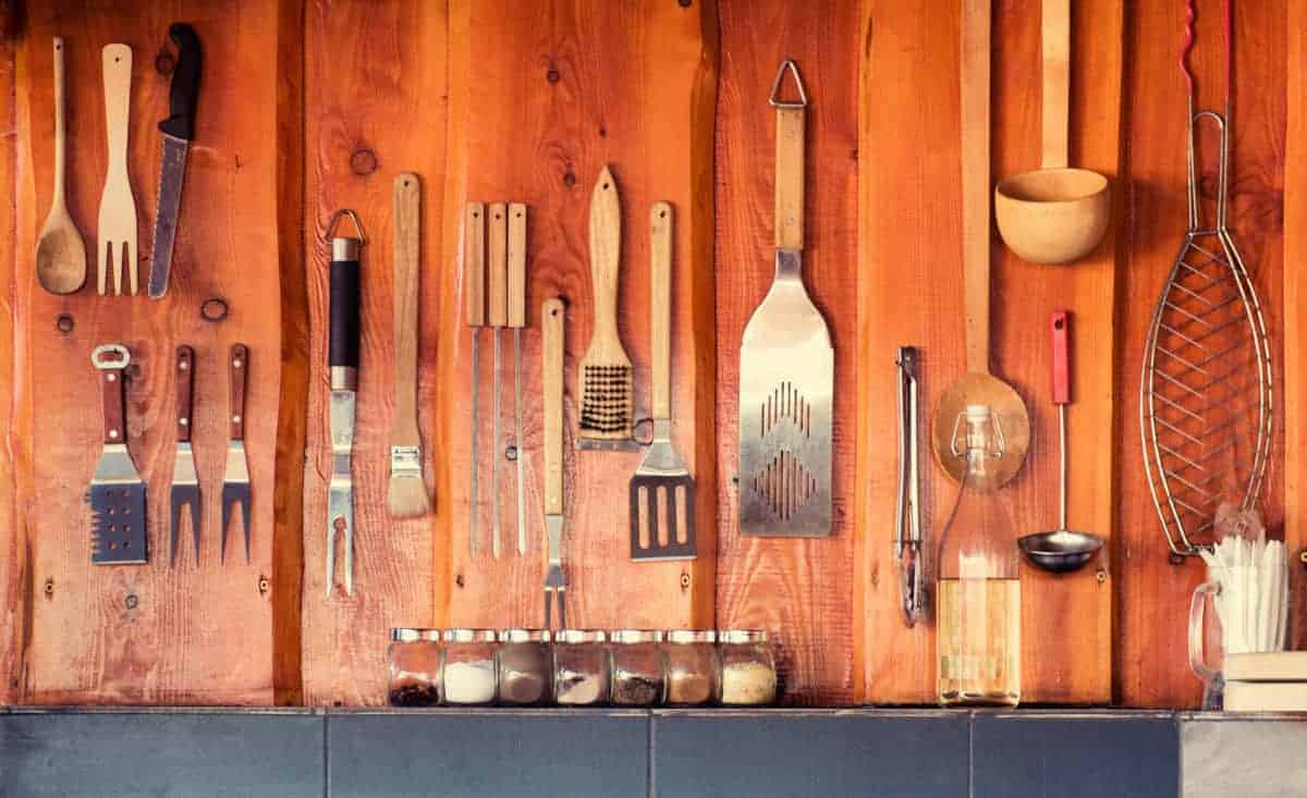 A wide angle shot of a BBQ tools collection hanging from a wooden w.