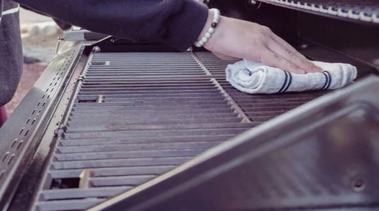 A man cleaning down some grill grates with a small towel.