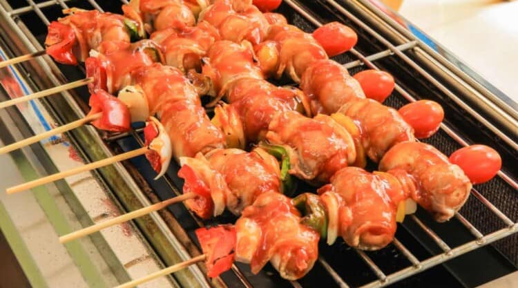 Bacon wrapped sausages on sticks, cooking on an infrared grill