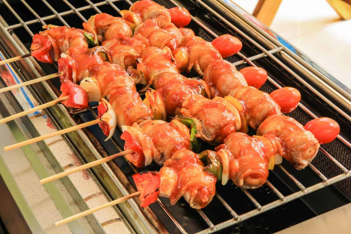 Bacon wrapped sausages on sticks, cooking on an infrared grill