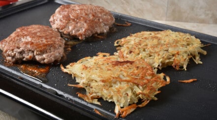 Sausage patties and hash browns on an electric griddle.