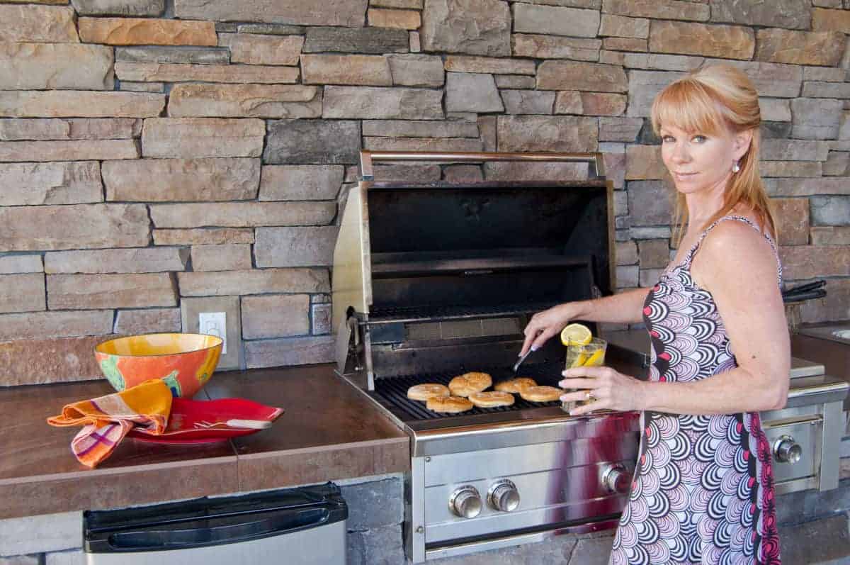 A woman cooking burgers on a natural gas gr.