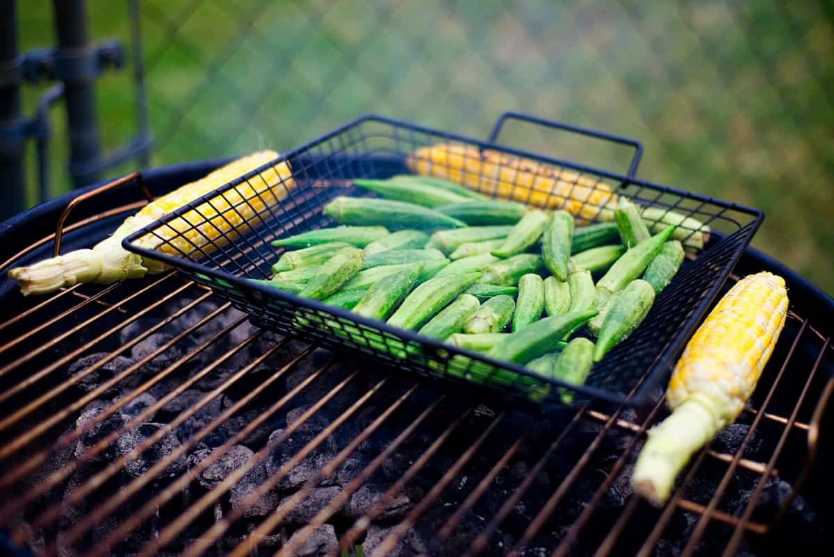 Corn and okra in an open grill basket over hot coals