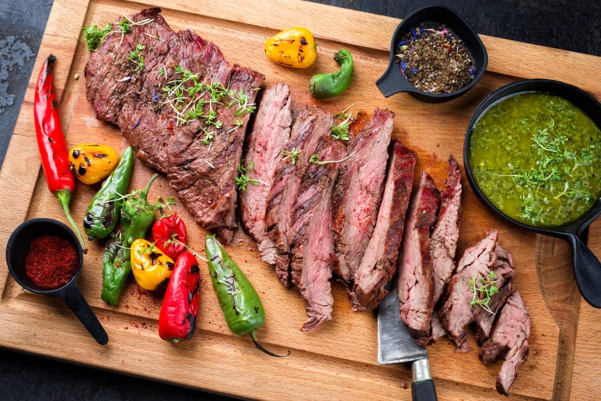 Grilled bavette with salsa verde and grilled peppers on a cutting bo.