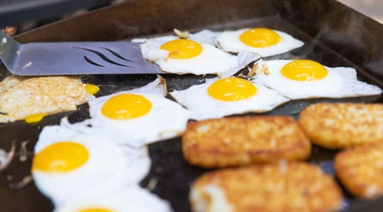 Eggs and hash browns cooking on an outdoor griddle