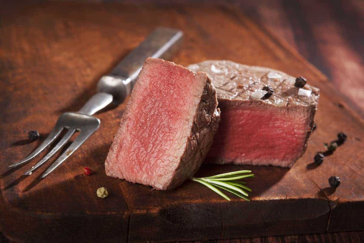 A cooked tenderloin filet mignon, sliced in half on a chopping bo.