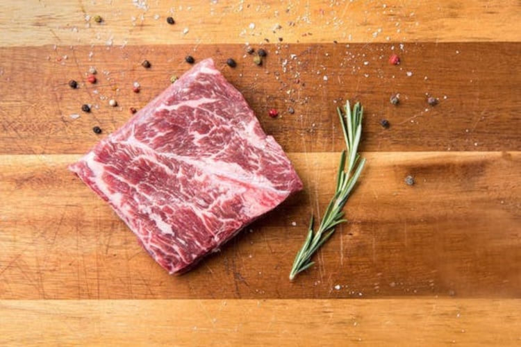 A flat iron steak from crowd cow, on a cutting board, next to a rosemary sp.