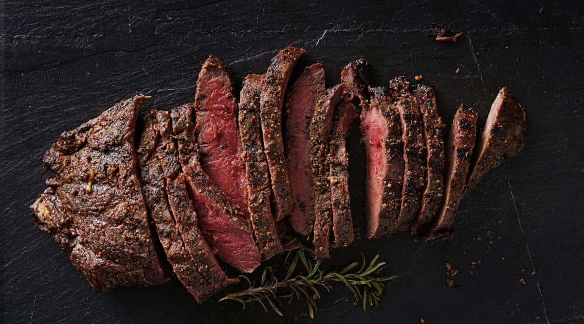 Grilled flat iron steak, sliced and on a black background.