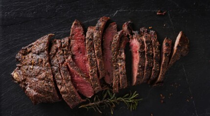 Grilled flat iron steak, sliced and on a black background.