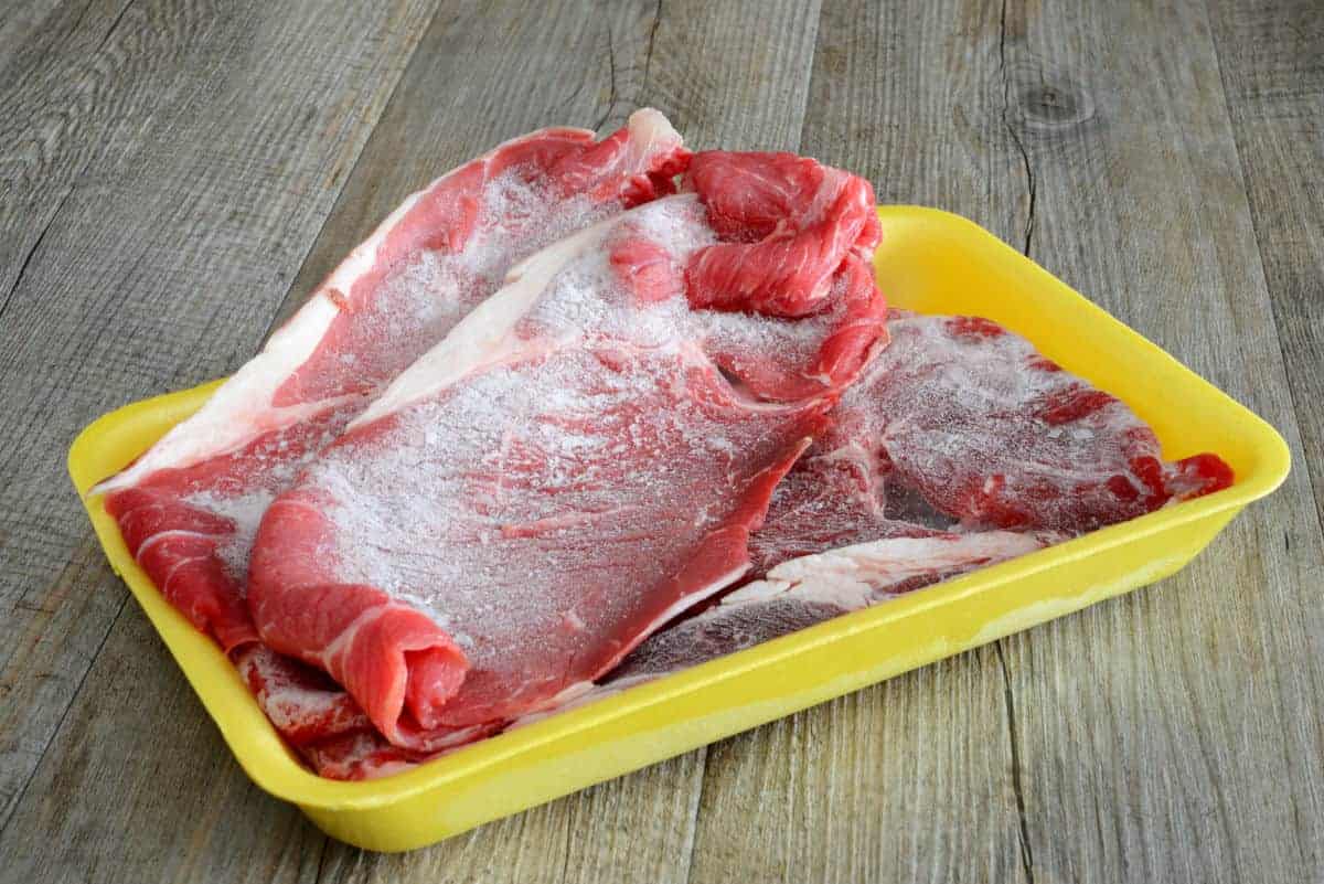 Frozen steaks in yellow tray showing signs of freezer b.