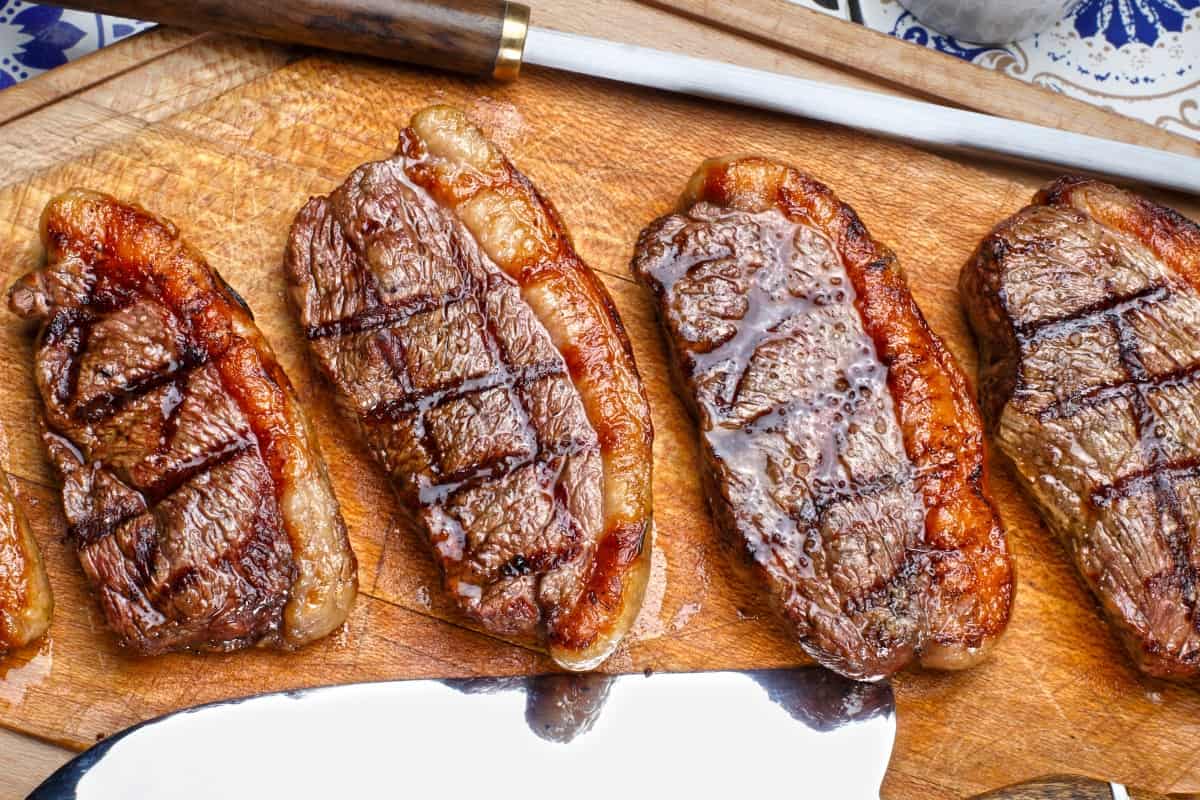 grilled picanha steaks laid out on a wooden cutting board with knife and sharpening st.