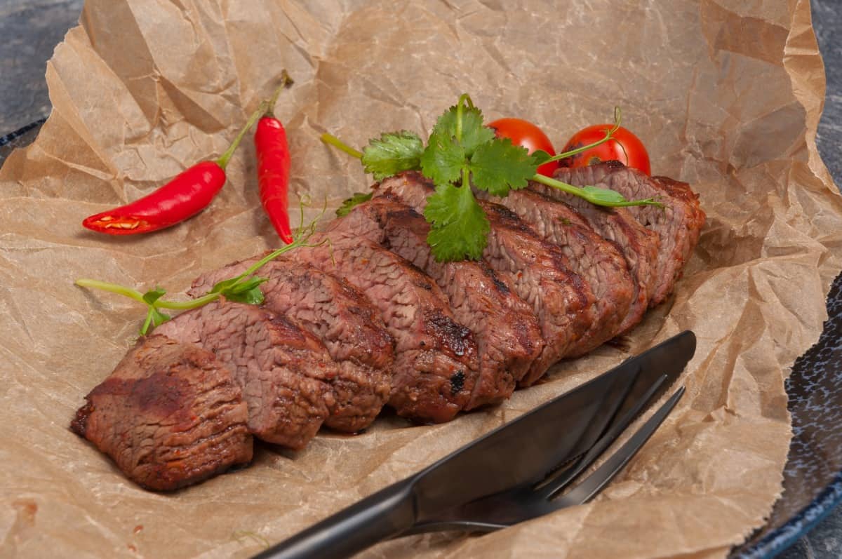 grilled shoulder steak on parchment paper with herbs, tomato and chi.