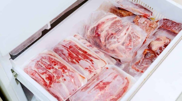 Plastic wrapped meat in the bottom drawer of a meat freezer.