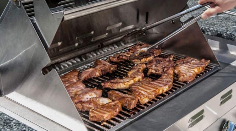 Steaks and small items of food being cooked on an infrared grill.