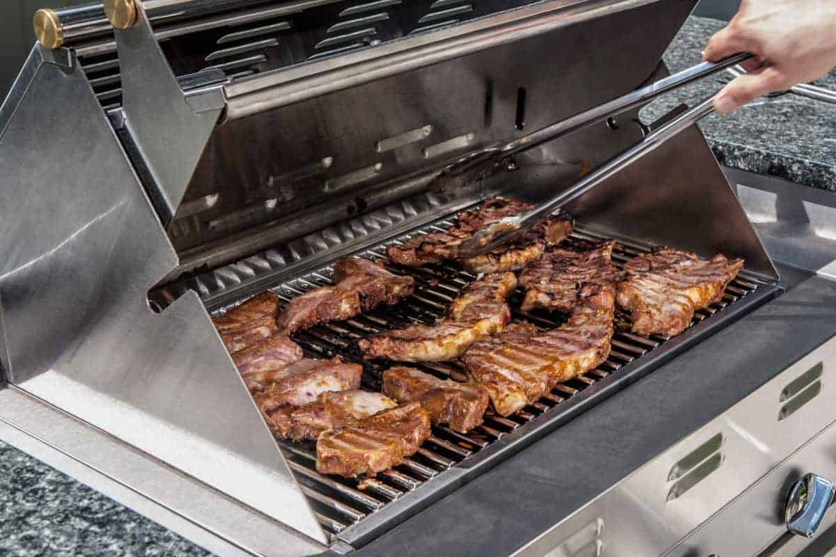 Steaks and small items of food being cooked on an infrared grill.