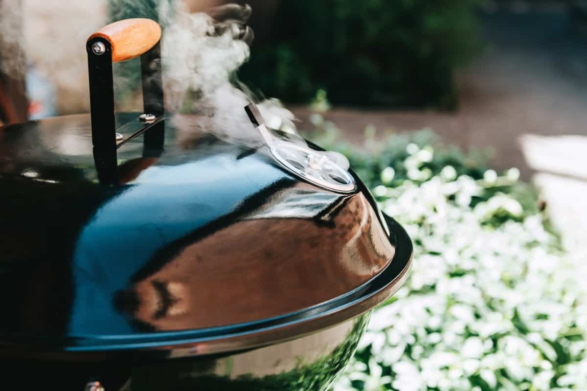 A charcoal kettle grill with lid on, smoke coming out from v.