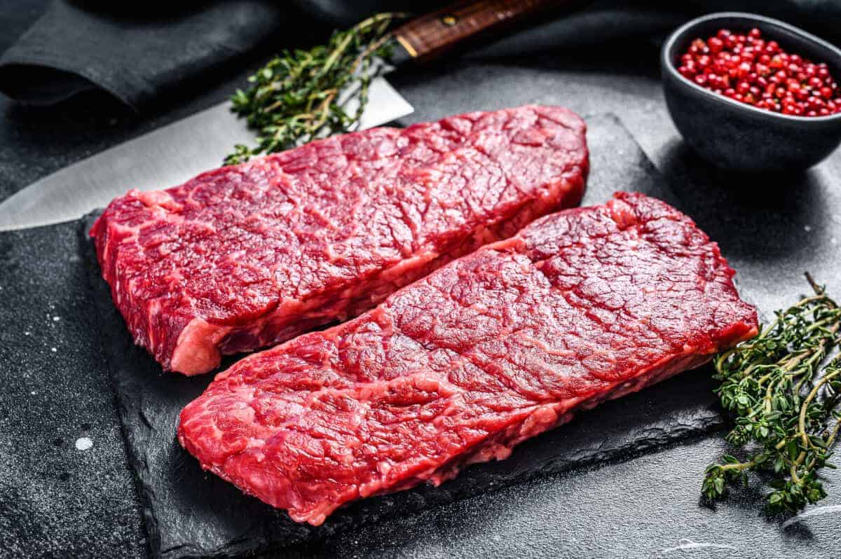 2 raw Denver cut steaks on a dark surface