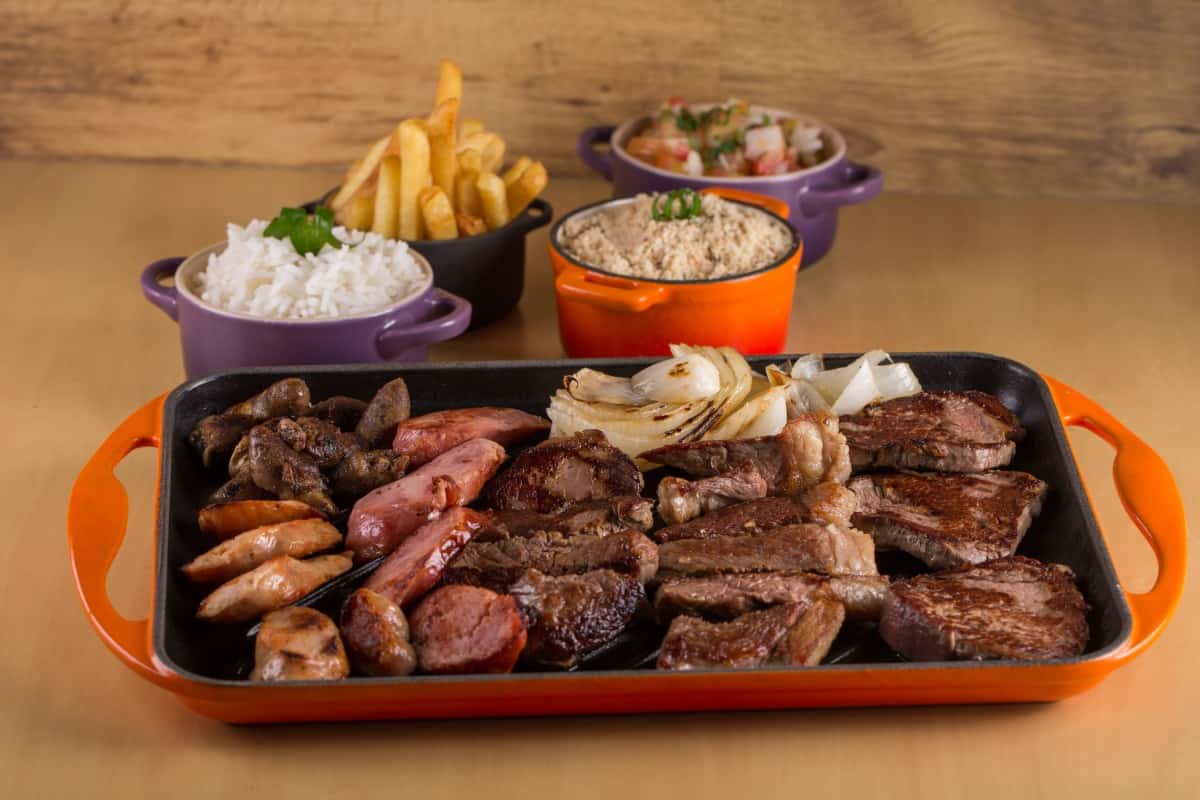 A churrasco platter of picanha, sausage, onion, chips and m.