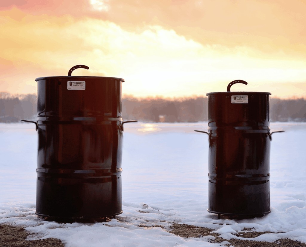Two pit barrel cookers on snow against a sunny background