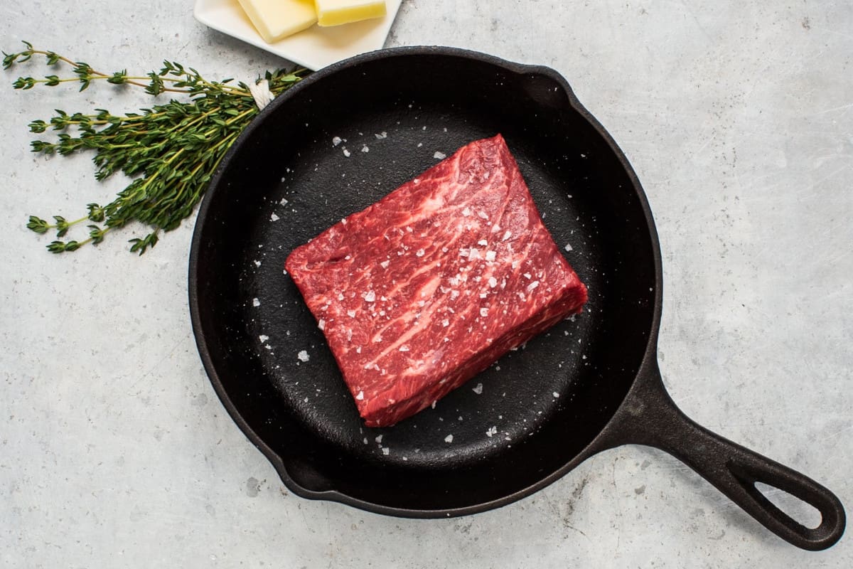 A Denver steak from Porter Road, in a cast iron skillet, next to some thyme sprigs, and a small bowl of but.