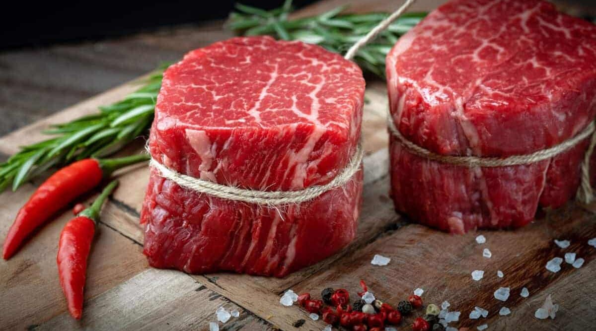 Two raw tenderloin filet mignon, tied on a chopping board.