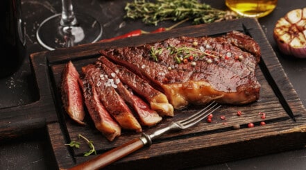 Sliced sirloin steak on a wooden chopping board with form and some herbs.
