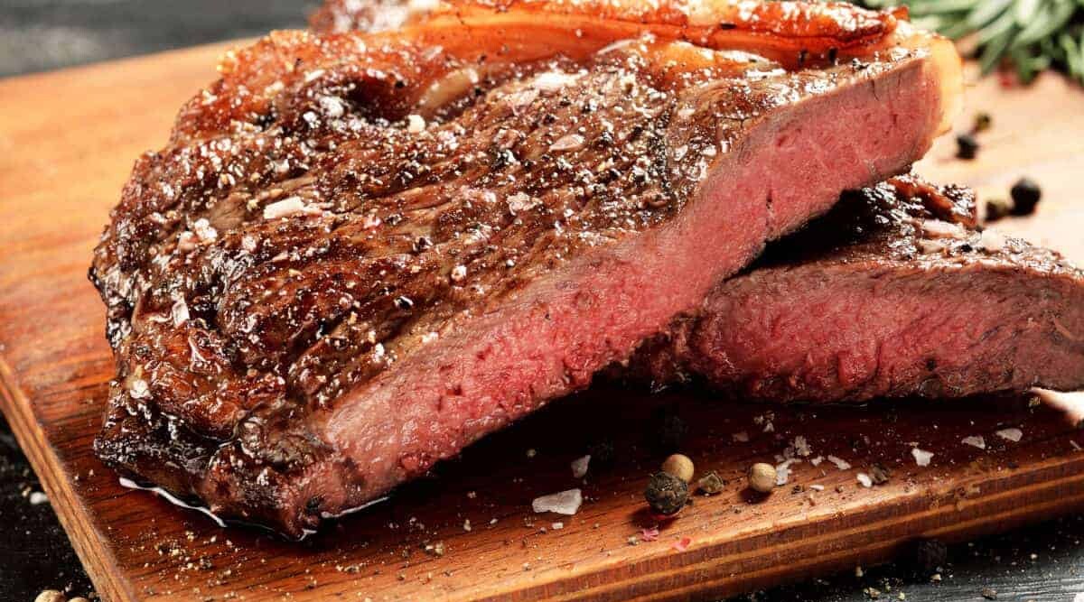 New York strip steak, cooked rare and sitting on a chopping board.