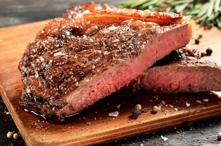 New York strip steak, cooked rare and sitting on a chopping board.
