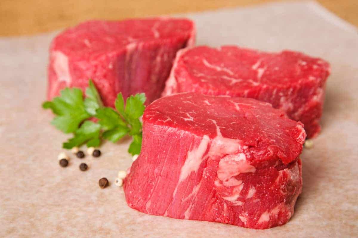 three raw beef tenderloin steak with parsley leaves and peppercorns