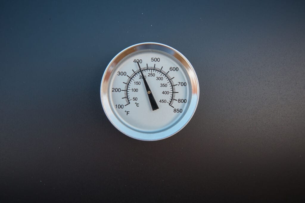 A close up of a smoker thermometer on a black barbe.