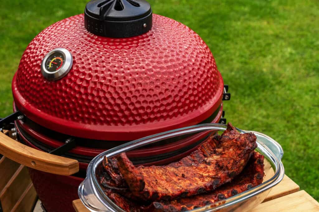 A red kamado grill with some rubbed ribs on it's side sh.