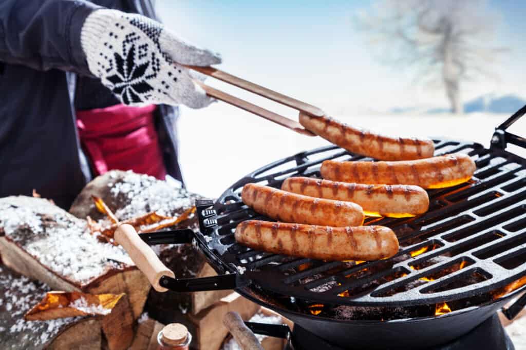 A person wearing BBQ gloves moving sausages around a hot gri.