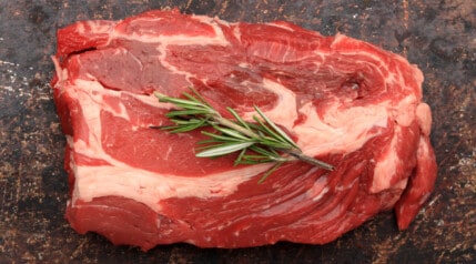 raw beef blade steak and rosemary on a dark surface.