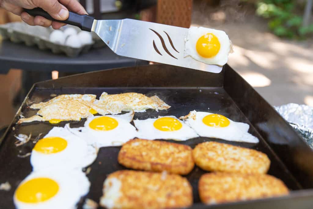 Breakfast of eggs and hash browns being cooked on a flat top griddle