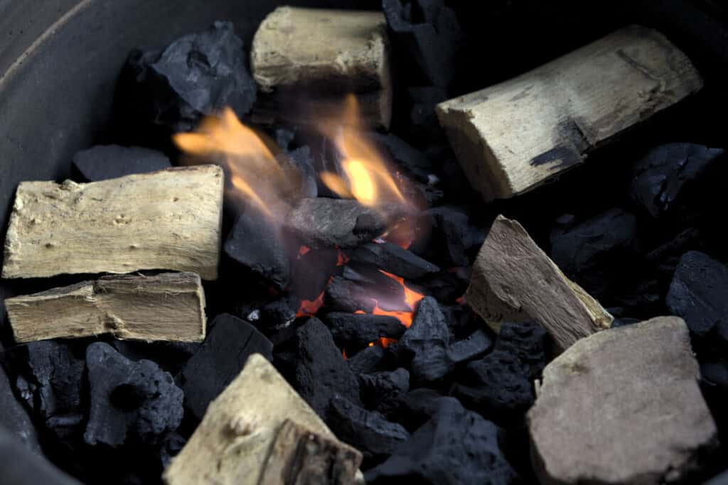 A close up of wood on top of smoldering charcoal inside a smo.